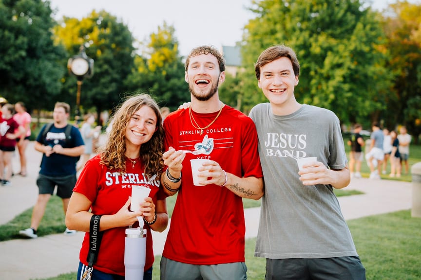 Three students smiling standing in front of trees and holding cups of ice cream
